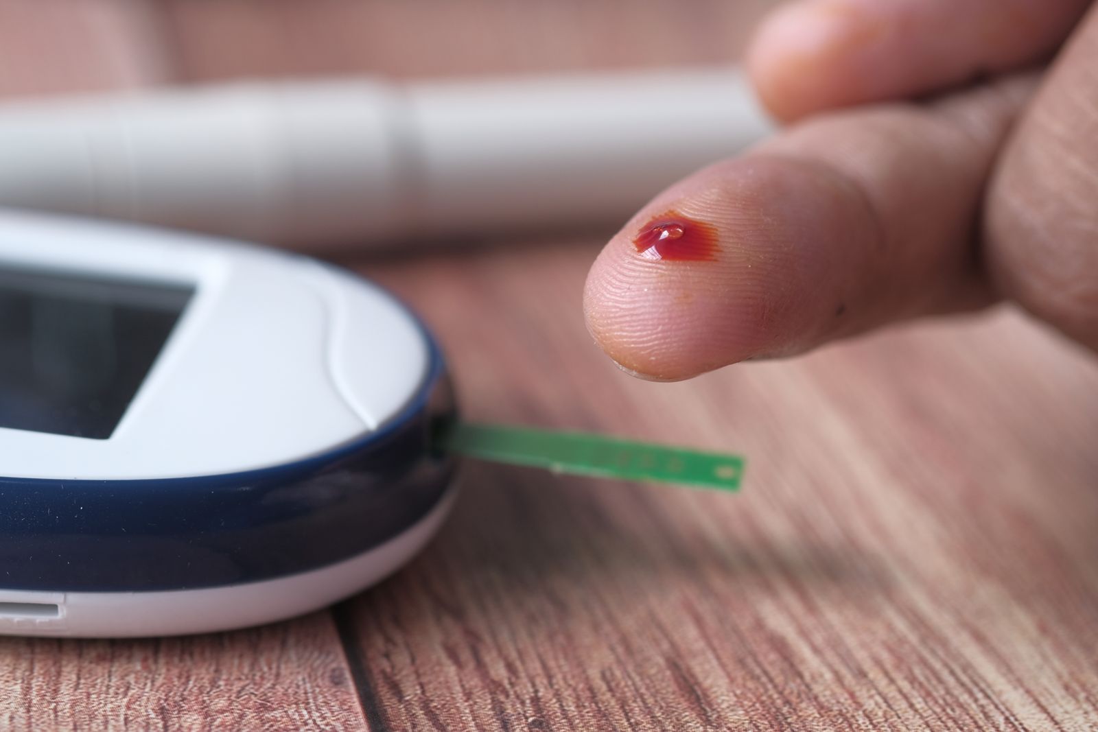 A blood glucose meter beside a pricked finger