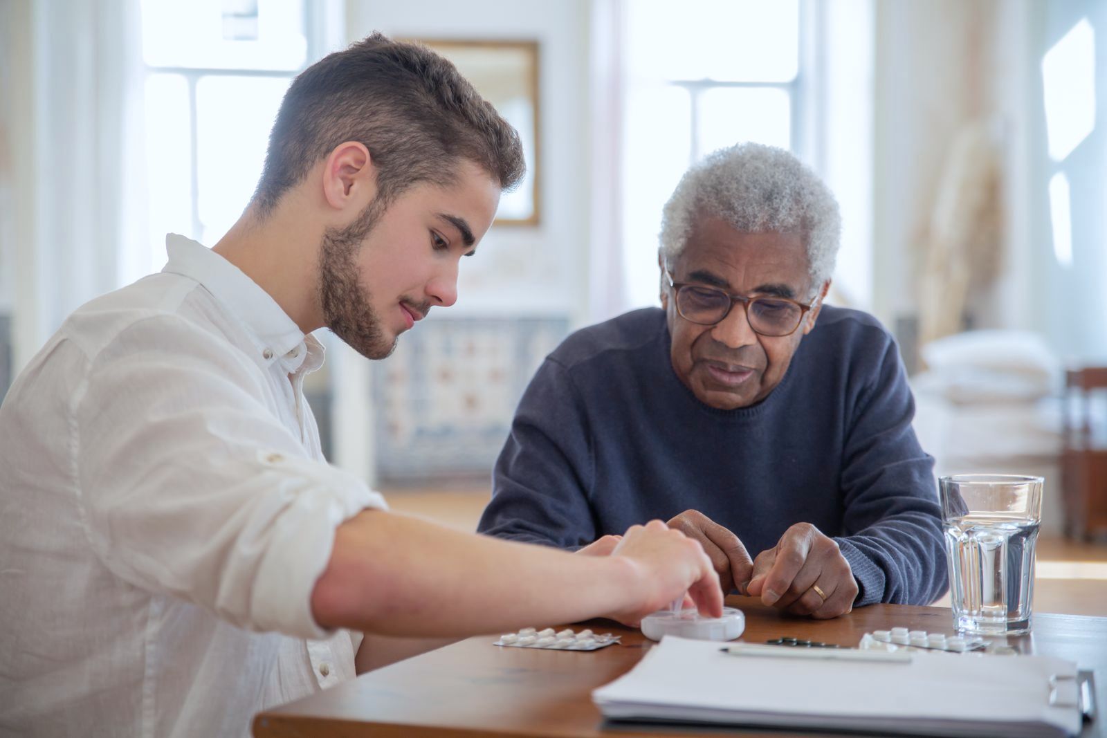 A young man helping an older man with his medication