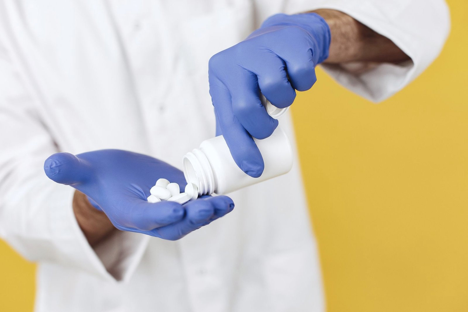 Gloved hands pouring tablets from a bottle