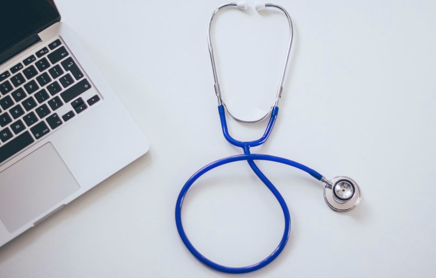 A laptop and stethoscope on a white desk