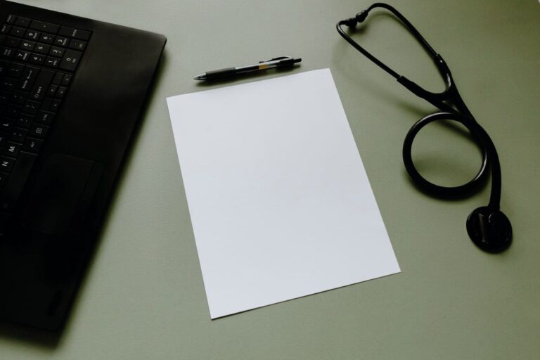 A laptop, pen, paper and stethoscope on a desk