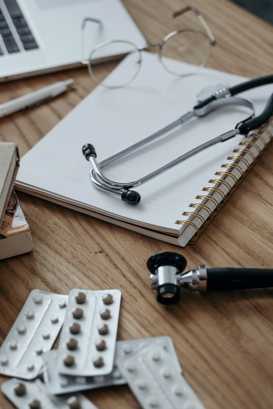 A notebook, stethoscope and blister packs on a desk