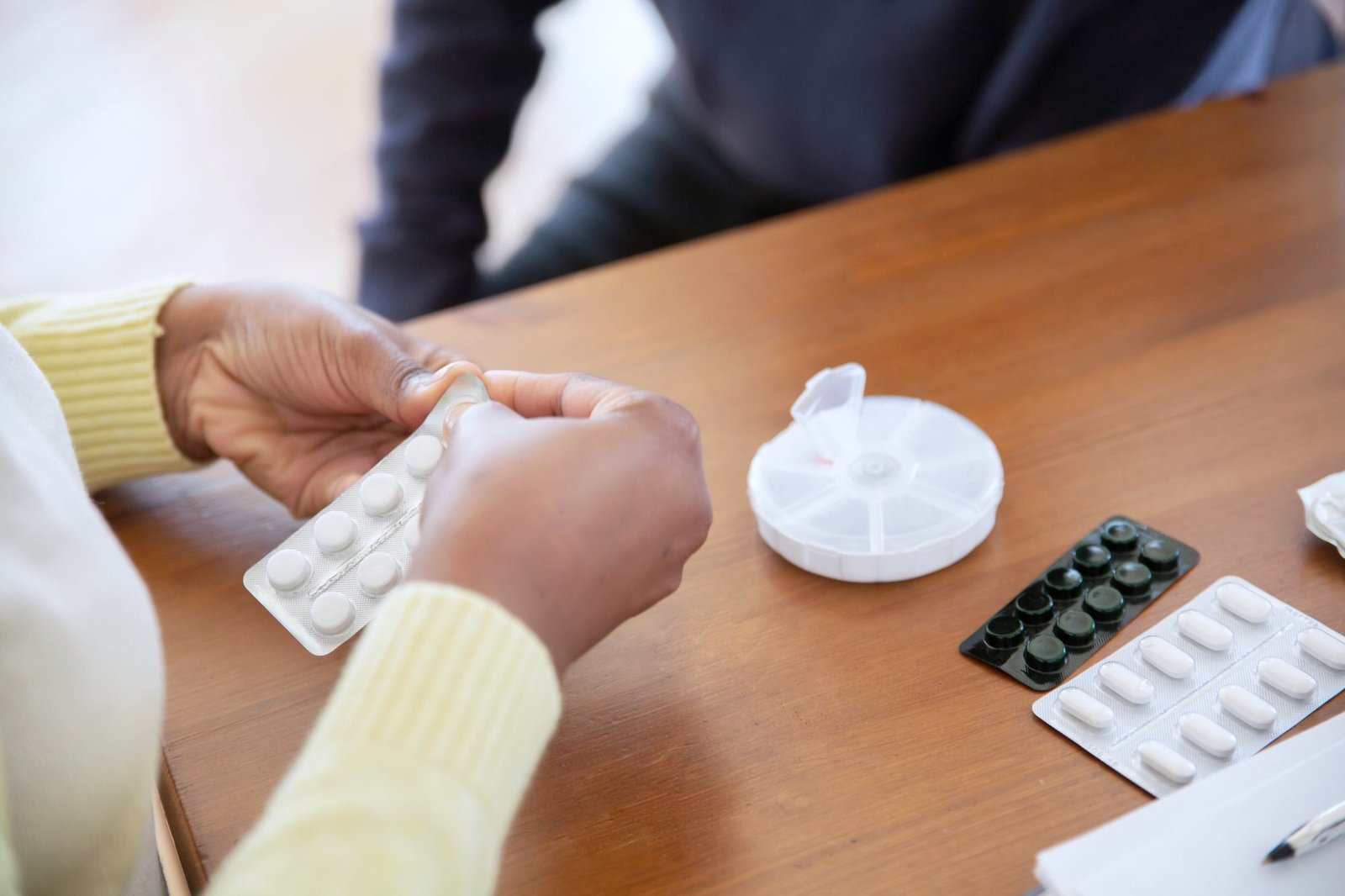 Two people going through blister packs and a pill organiser at a table